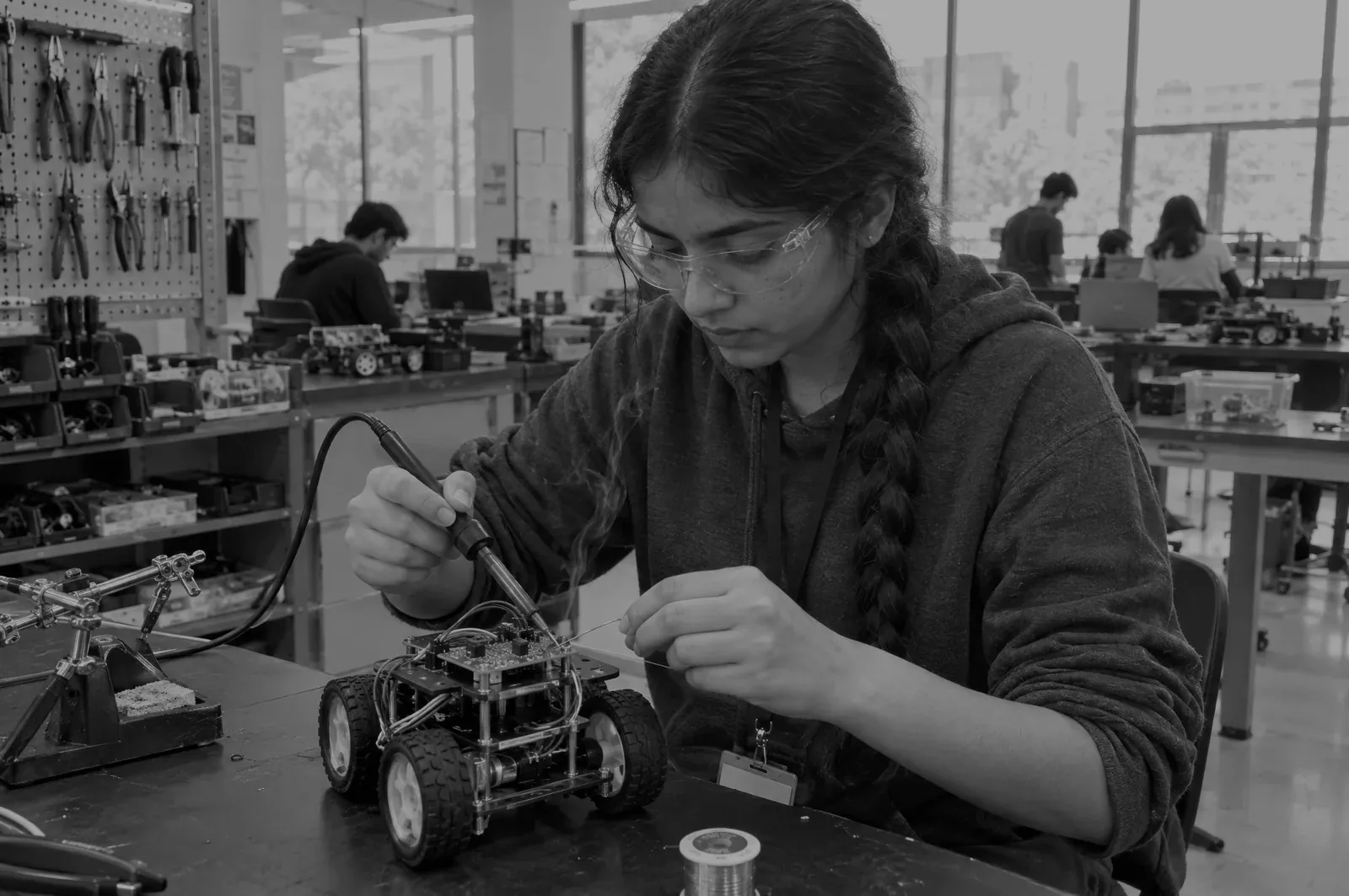 A student in safety glasses soldering a circuit board on a robot kit